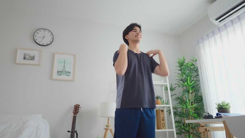 Asian young handsome sportsman excercise in cozy living room at home. Attractive male in sportswear spends free leisure time workout and stretching body on holiday in house. Healthy lifestyle concept.