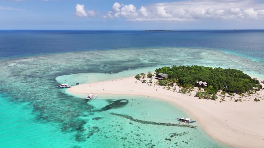 Aerial view of Patawan Island featuring pristine white sand beaches, turquoise waters, coral reefs, and lush green foliage in Balabac, Palawan, Philippines, with traditional boats near the shore
