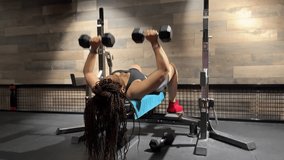 A woman performs a dumbbell bench press on a flat bench. The camera slowly moves forward, reframing as she lifts and lowers the dumbbells. - Powered by Shutterstock - Get 15% off with code: PIKWIZARD15