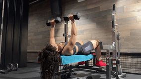 A woman lies on a bench and performs multiple dumbbell chest presses, lifting and lowering the weights over her face. - Powered by Shutterstock - Get 15% off with code: PIKWIZARD15