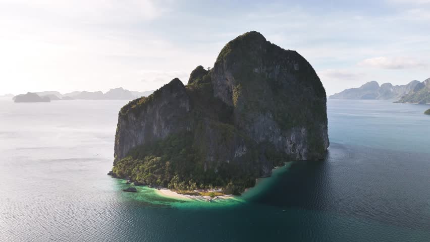Drone orbiting Pinagbuyutan Island in El Nido, Palawan, revealing dramatic limestone formations, dense foliage, and turquoise waters of the Bacuit Bay in the Sulu Sea