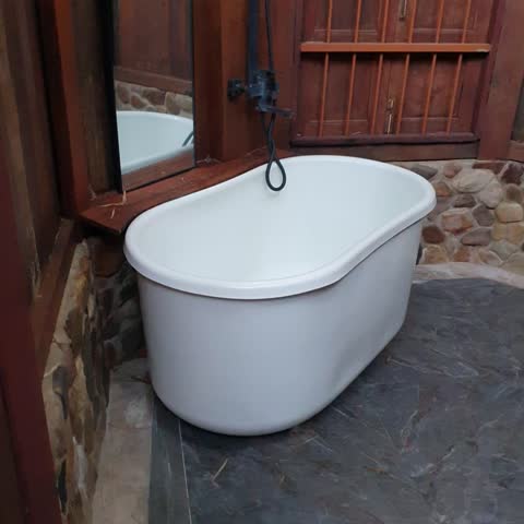 This video a vintage wooden bathroom with an open roof, bamboo view, bringing nature inside. Featuring a white bathtub, shower, and string lights, creating a serene, natural ambiance.