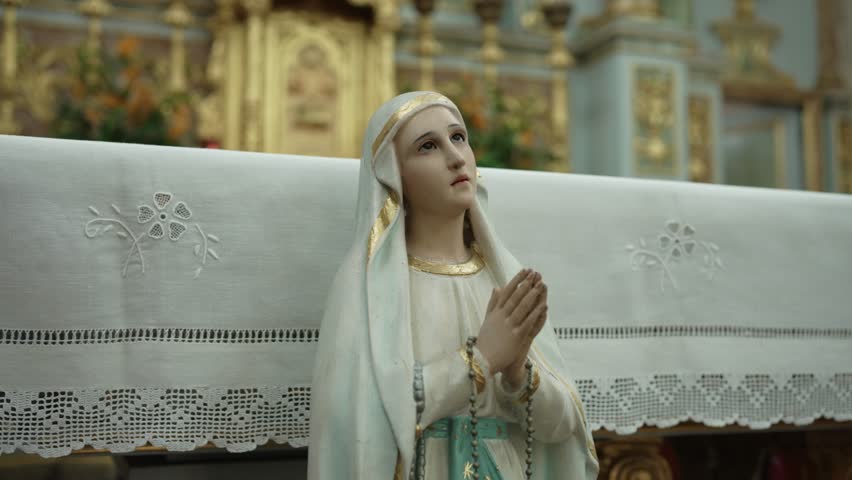 close up of Virgin Mary statue with folded hands and rosary before ornate altar