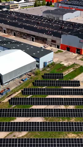 Modern industrial complex powered by extensive ground-mounted solar panels, emphasizing renewable energy - vertical aerial reveal