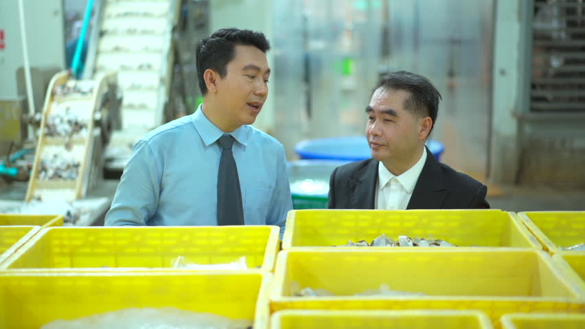 Two Asian businessmen walk through a seafood and canned fish processing factory, inspecting raw materials and shaking hands. The moment represents partnership, and business collaboration. - Powered by Shutterstock - Get 15% off with code: PIKWIZARD15