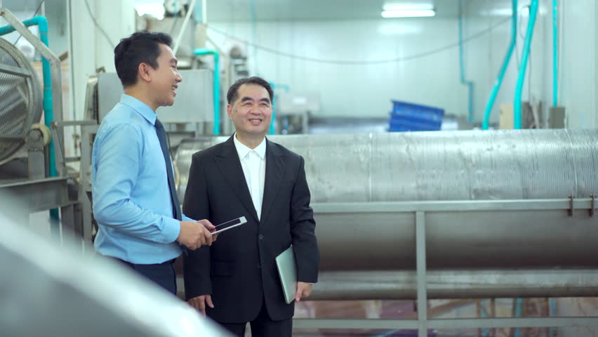 Two Asian businessmen walk through a seafood and canned fish processing factory, inspecting raw materials and shaking hands. The moment represents partnership, and business collaboration. - Powered by Shutterstock - Get 15% off with code: PIKWIZARD15