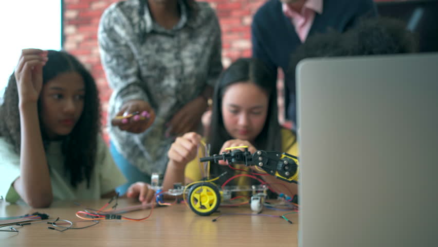 group of diverse high school students learns about programming and electronic robot components in a STEM class, with a teacher guiding them closely in an interactive learning environment. - Powered by Shutterstock - Get 15% off with code: PIKWIZARD15