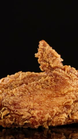 Golden-brown fried chicken wings rotate smoothly under studio lighting, highlighting crunchy texture and juicy details against a clean, black backdrop with subtle reflections