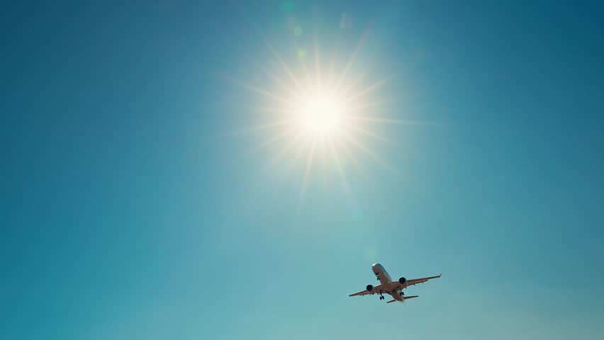 Passenger airplane flying across blue sky with sun behind wings, symbol of freedom, speed, modern aviation and global travel