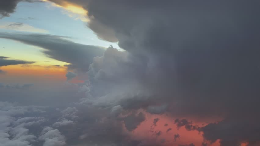 an aerial view from a plane cockpit while flying close to a raging thunderstorm with lightning strikes and rain, with the orange sunset light breaking through the clouds. Handheld camera. 4K