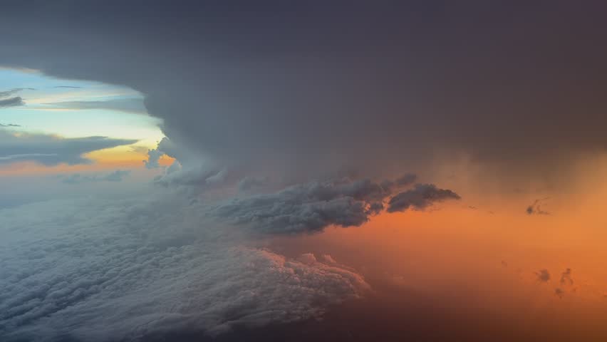 An aerial view of a massive and vilolent storm cumulonimbus cloud at sunset, with golden hour light breaking through amber haze and rain. An aerial view from a jet cockpit. Handheld camera.