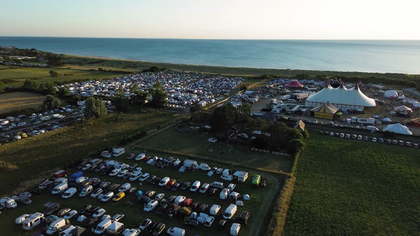 Drone footage reveals the expansive camping grounds of the Chauffer dans la noirceur festival in Normandy, illuminated by the warm tones of sunset.