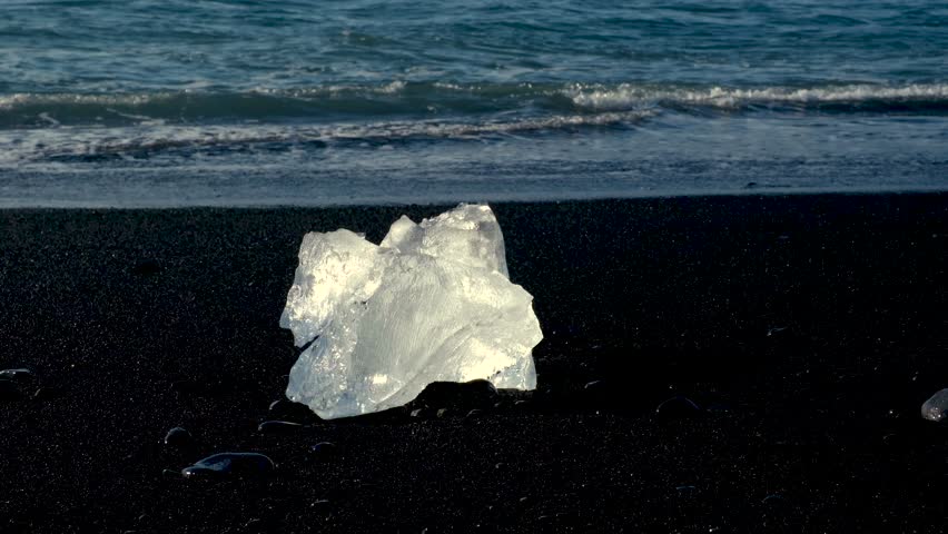 Crystalline chunks of ice rest upon the striking black sands of Diamond Beach, reflecting sunlight against the waves of the Atlantic Ocean, creating a stunning coastal vista in Iceland