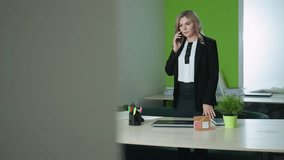 CEO on call with client opens laptop to start work in modern office with architectural model on desk, green accent wall, file shelves and organized workspace in background - Powered by Shutterstock - Get 15% off with code: PIKWIZARD15