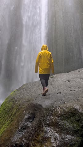 Discover the breathtaking Gljufrabui canyon Iceland waterfall as a traveler walks along the rocky path, wearing a vibrant yellow rain jacket. Mist fills the air, creating an enchanting atmosphere.