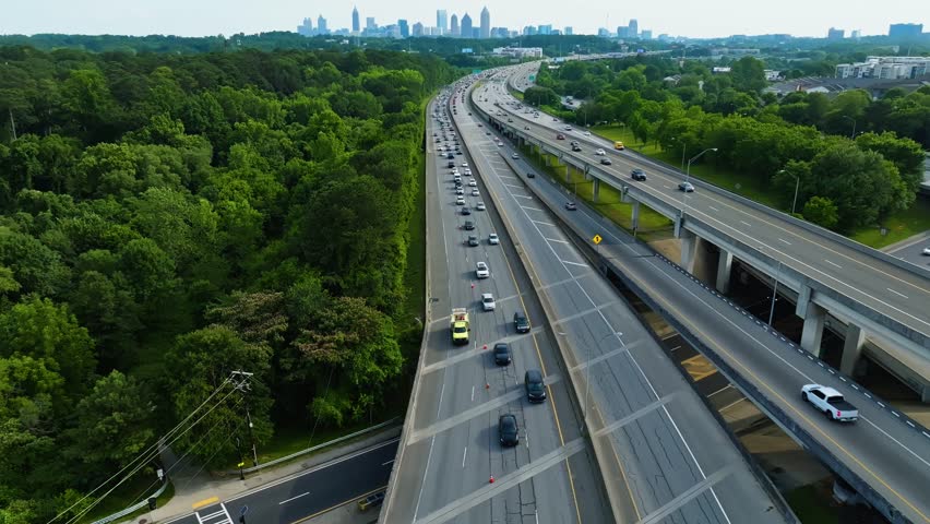 Interstate highways with traffic in rural area. Skyline silhouette with skyscraper in Atlanta, Georgia. Aerial wide shot. Traffic jam and green forest trees in summer.