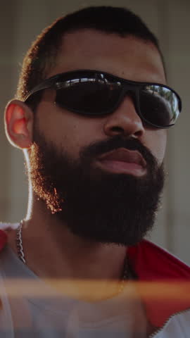 Bearded African American man takes off stylish glasses standing under urban overpass bridge. Cool black guy expresses spirit of modern hip hop culture in city