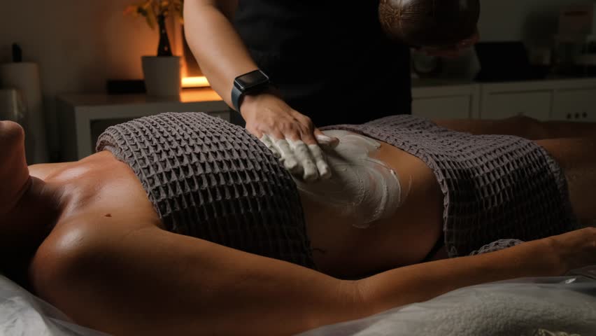 Rejuvenating and relaxing massage with application of a cream mask on a woman's body in a spa salon.