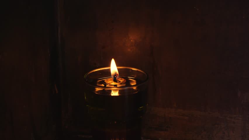 Lit candle in a glass holder glows warmly on dark wood inside a church in Elefsina, Greece. The flame flickers in deep darkness, casting soft orange light. No people - Powered by Shutterstock - Get 15% off with code: PIKWIZARD15