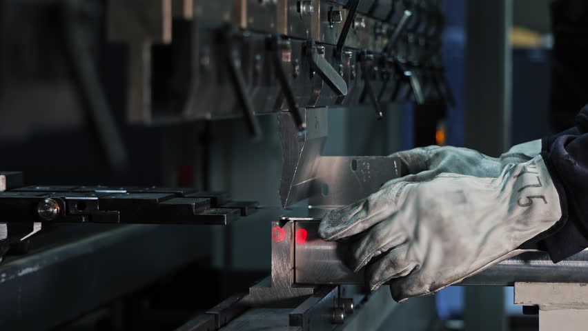 Industrial sheet metal bending with press brake. Factory worker using a press brake machine to accurately bend a metal sheet under controlled pressure and alignment lasers.