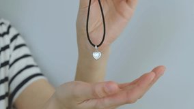 A person is holding a necklace with a heart pendant. The necklace is black and silver. The person is wearing a white shirt - Powered by Shutterstock - Get 15% off with code: PIKWIZARD15