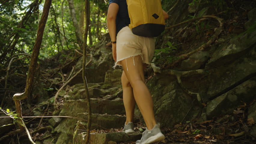 Woman Climbing Stone Steps Surrounded by Jungle Vines and Trees Wearing Backpack and Sneakers, Low Angle, Adventure and Effort Concept.