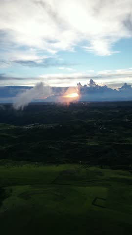 Aerial drone footage flying above the rolling hills of Meghalaya, India, during golden sunset, showcasing dramatic skies, clouds, and lush green terrain glowing in evening light