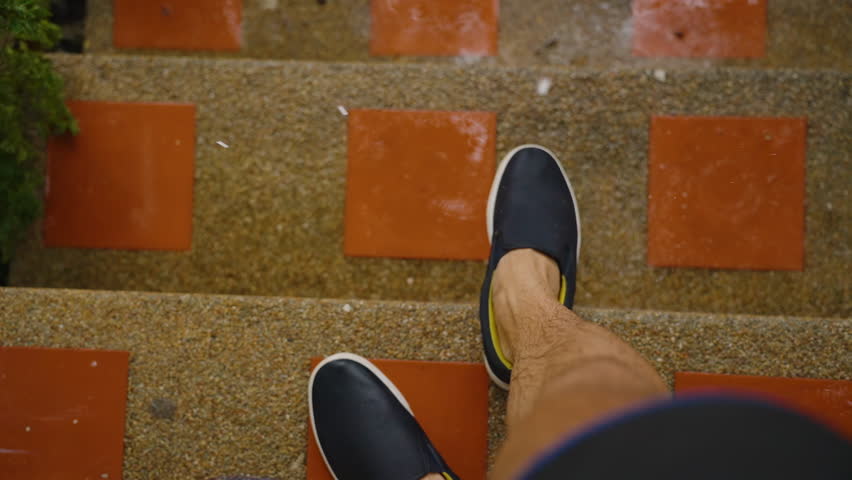 View of Wet Legs and Black Shoes on Stairs During Rain with Water Droplets Falling Around in Slow Motion, Tropical Downpour Concept.