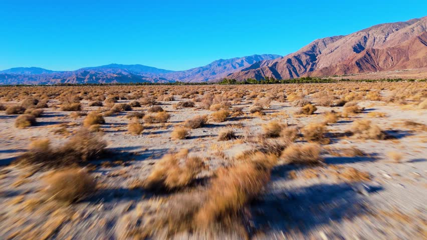 Fast flyover above desert valley with dry bushes