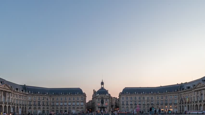 Place de la Bourse day to night transition panoramic timelapse in Bordeaux, France, reflecting illuminated architecture. Landmark and the fountain with traffic and tram passing by