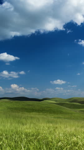 Green grassy hills under blue sky with fluffy white clouds floating above