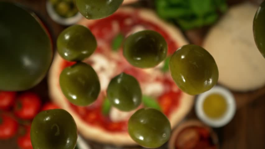 Super slow motion of falling green olives on pizza dough with camera follow and rotation . Filmed on high speed cinema camera , 1000 fps