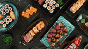 Top view of traditional japanese cuisine . Sushi rolls set with salmon , tuna fish and vegetable served on black stone table . Asian food on black stone slate with chopsticks . Camera movement . - Powered by Shutterstock - Get 15% off with code: PIKWIZARD15