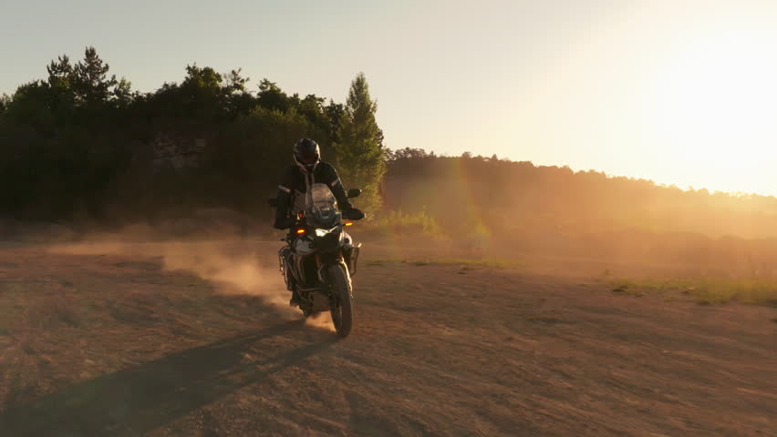 Slow motion shot of a rider on a motorcycle riding in dusty terrain