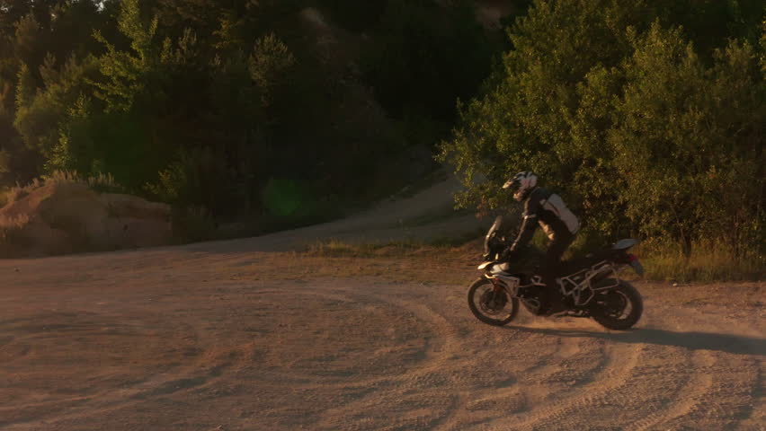 Slow motion shot of a rider on a motorcycle riding in dusty terrain