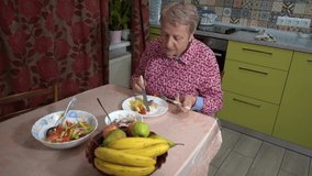An elderly woman eats fish and vegetables on a plate with a knife and fork. A grandmother is having lunch at home in the kitchen. Healthy eating. Bananas on table - Powered by Shutterstock - Get 15% off with code: PIKWIZARD15