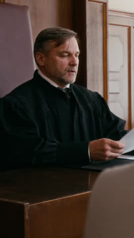 Vertical shot of middle-aged male judge sitting at beach and reviewing documents before start of trial in courtroom