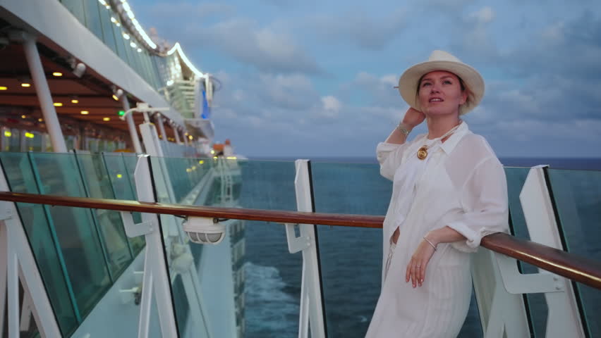 A stylish woman in an elegant white outfit and trendy hat poses gracefully on a luxurious cruise ship deck, enjoying a breathtaking ocean view at sunset, capturing an unforgettable travel moment
