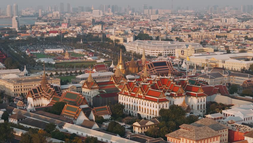 Aerial view of Bangkok Grand palace surrounded by urban skyline under a warm sunset glow, Thailand