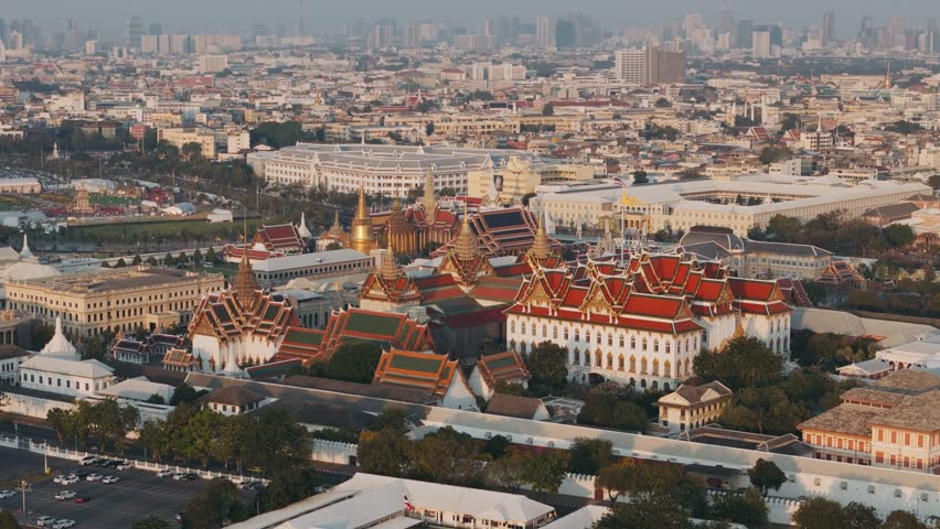 Aerial view of Bangkok Grand palace surrounded by urban skyline under a warm sunset glow, Thailand