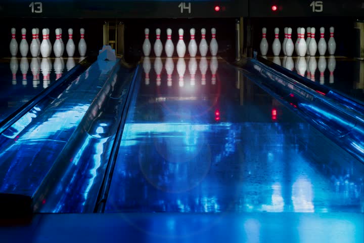 Zooming in on bowling lanes in a modern bowling alley. Ten bowling pins zoom close up. Slow moving background. Blue lighting