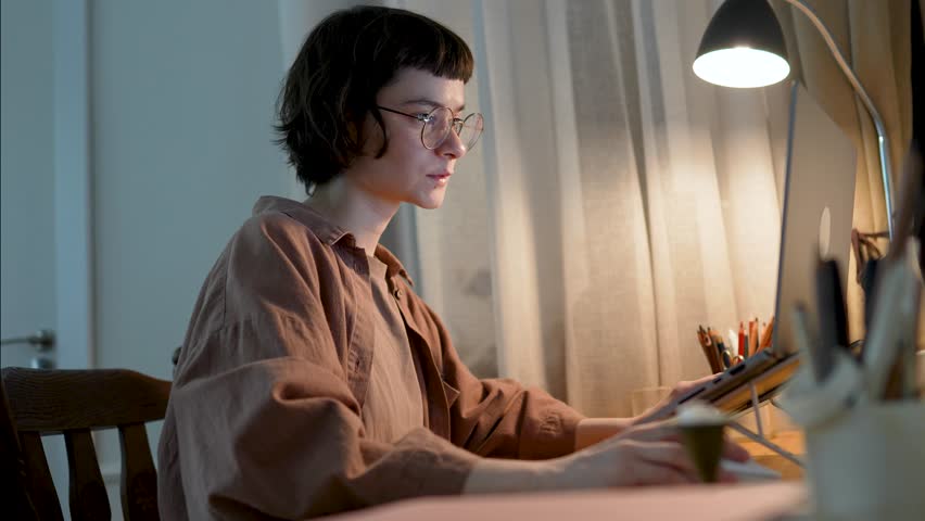 Young woman deeply focused on laptop working from home. Remote work, freelance digital nomad career, online education, flexible schedule, long screen time, mental load, digital workflow, burnout risk