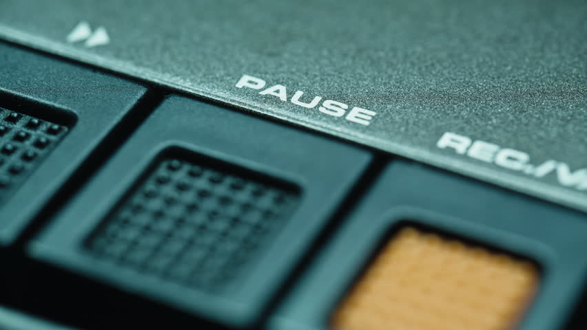 Finger pressing pause button on retro tape player closeup. Thumb touching faded playback panel of classic recorder indoors. Unknown user operating audio equipment inside quiet recording room place