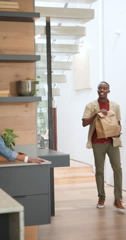 African American couple entering kitchen holding bag unpacking drinks and boxes as tapping phone. Domestic, lifestyle, modern, casual, family, home, vertical video