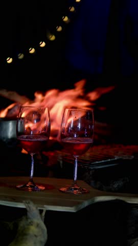 Wine glasses standing on a wooden board near a burning fireplace create a romantic atmosphere