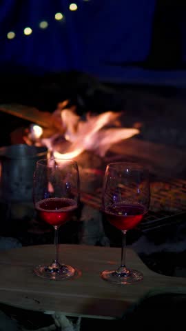 Friends celebrating, raising glasses of red wine near a campfire at night