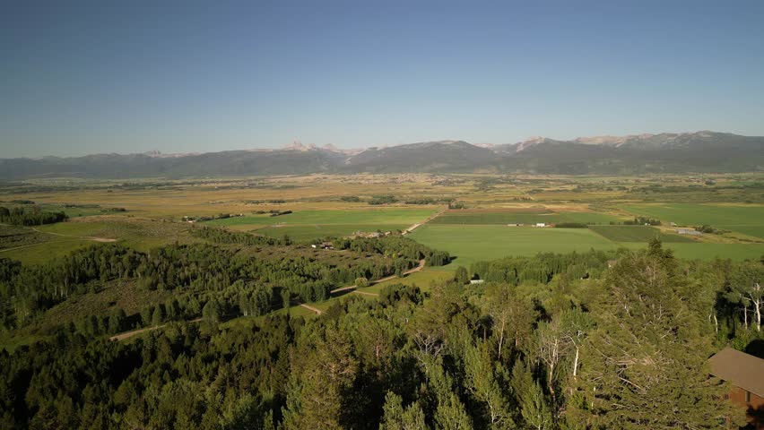 Aerial above forested mountain homes in Victor Idaho in summertime with view of Tetons