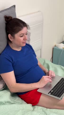 Caucasian woman sitting on bed typing on laptop. 