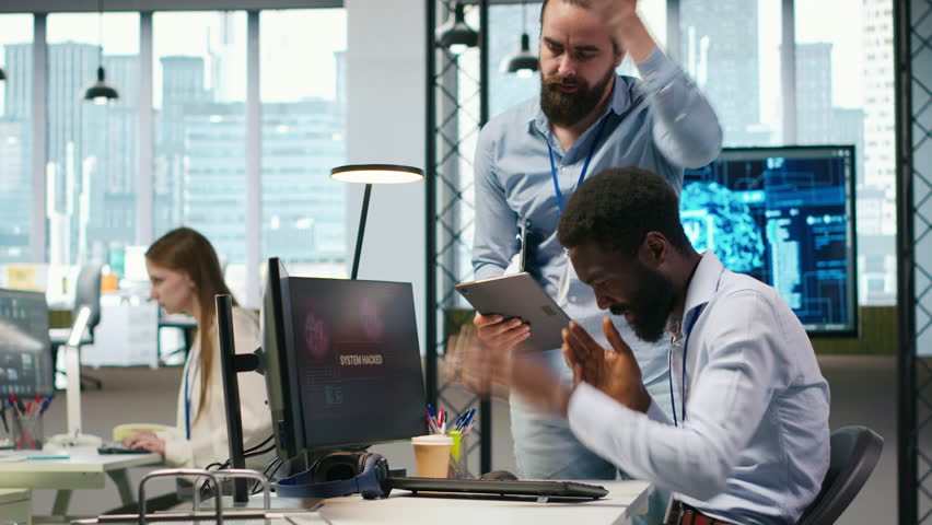 Programmer requests help from team leader to fix hacking attempt on corporate network. IT employee and manager investigating unauthorized access alerts, doing brainstorming, camera A