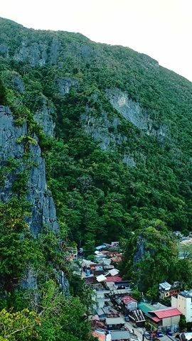 Steep rocky cliffs and dense vegetation rise above El Nido coastal community. Aerial shot of dramatic cliffs and jungle over village rooftops in El Nido, Palawan, vertical screen